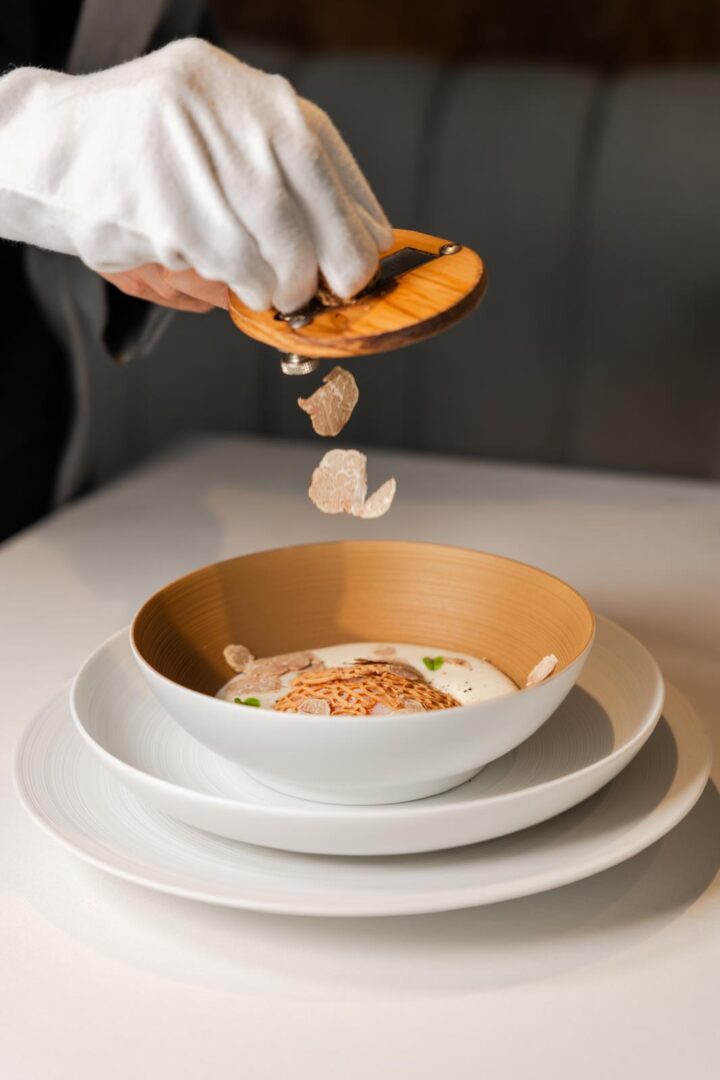 Waiter in white gloves shaving white truffle over an egg dish at Areia Marbella